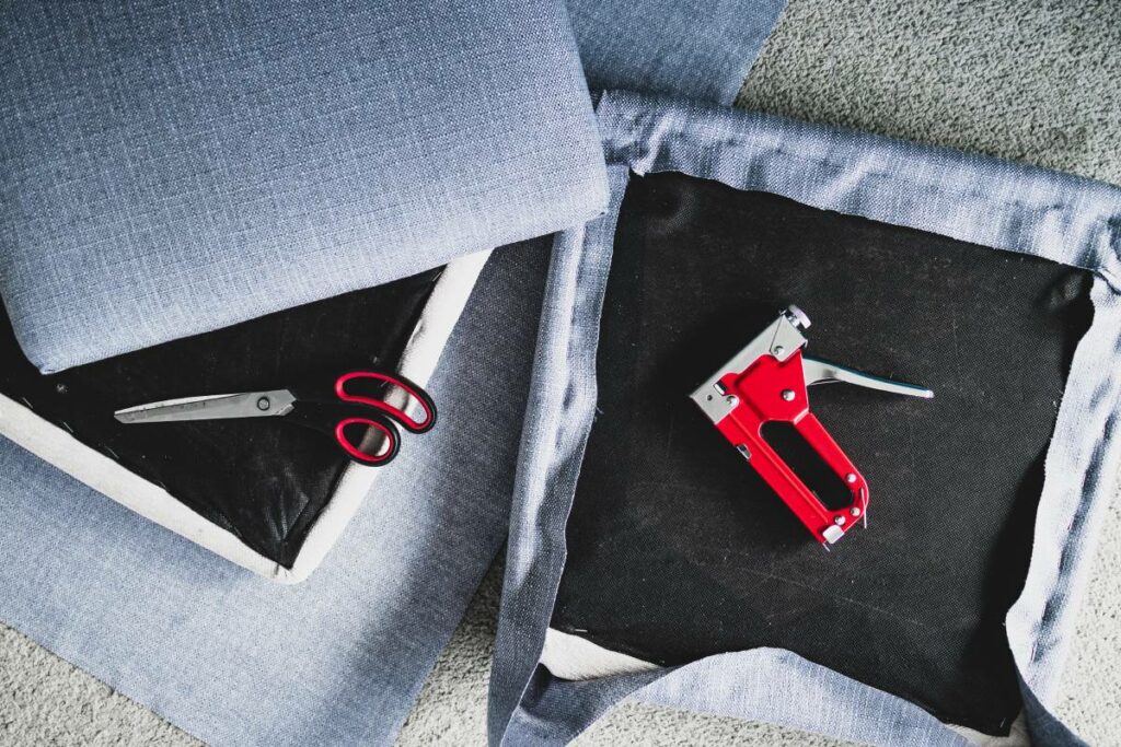 Three gray tweed chair cushions with scissors and a nail gun in an upholstering service.